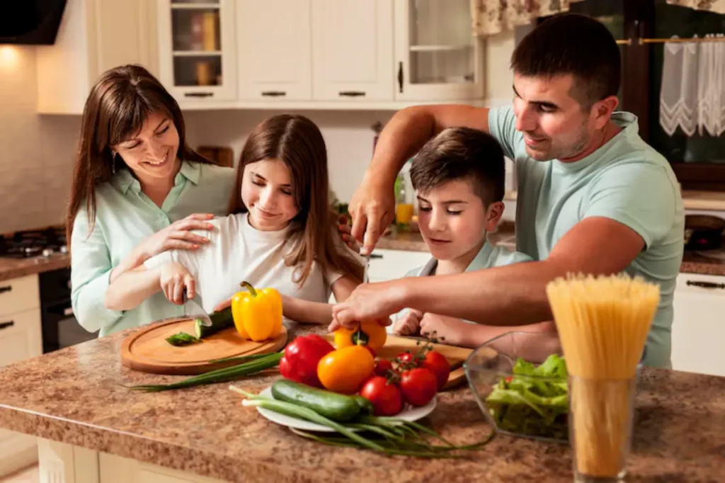 A family prepares a meal together in a bright kitchen, surrounded by fresh vegetables and cooking ingredients on a countertop.