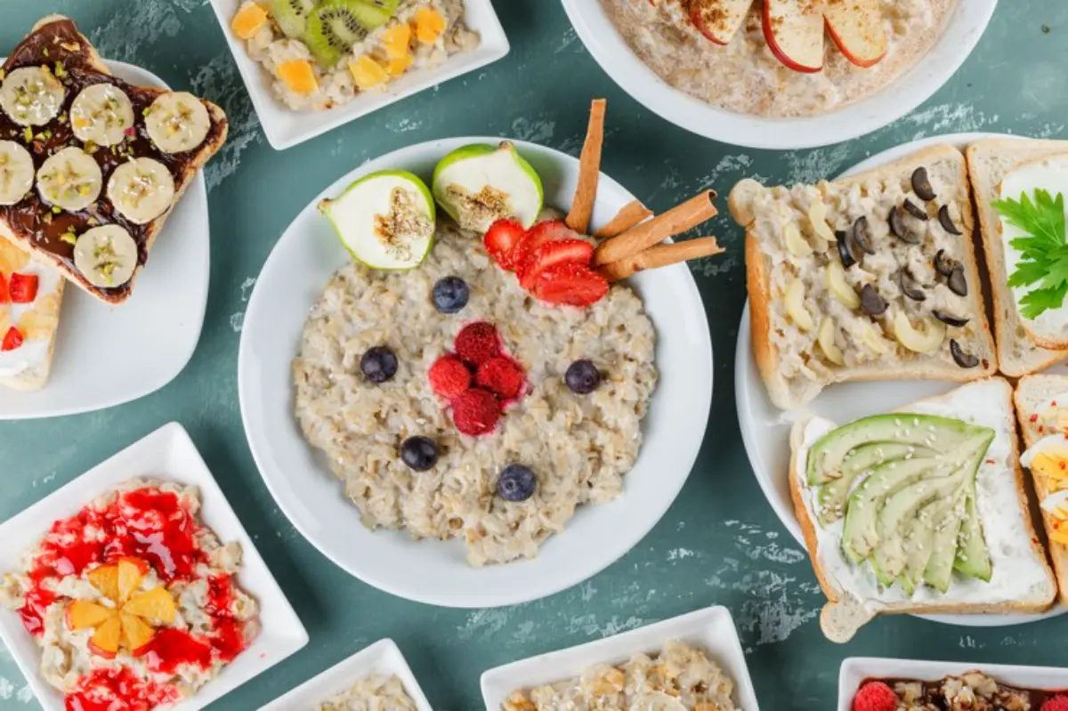 A variety of colorful breakfast dishes, including oatmeal with fruit, toast with toppings, and yogurt, arranged on a green background.
