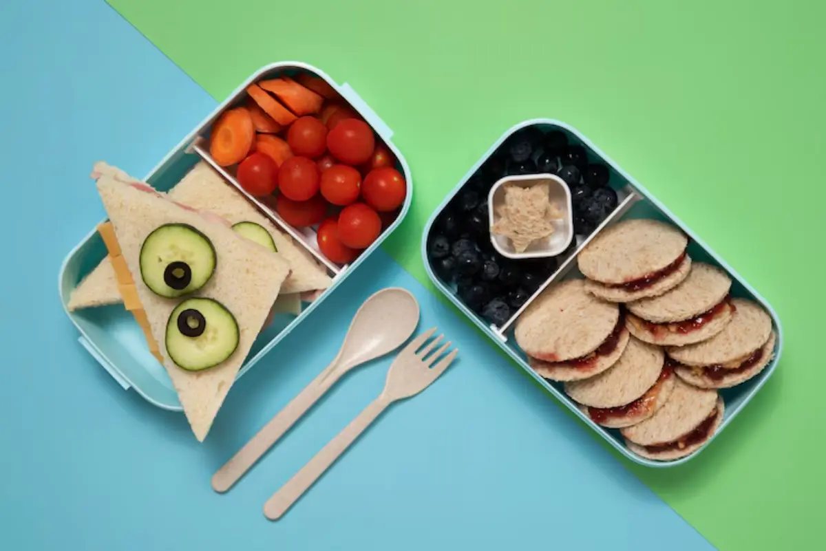 A colorful lunchbox filled with playful sandwiches, cherry tomatoes, carrots, blueberries, and mini peanut butter sandwiches.