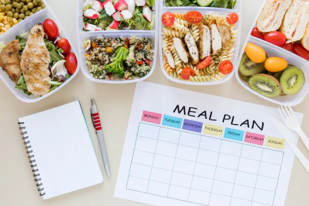 A variety of meal prep containers with salads, chicken, and fruit, alongside a blank meal plan and a notebook on a table.