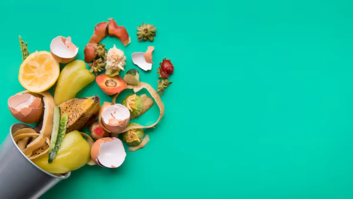A bucket spills colorful food scraps including fruit peels, eggshells, and vegetable remnants against a bright turquoise background.