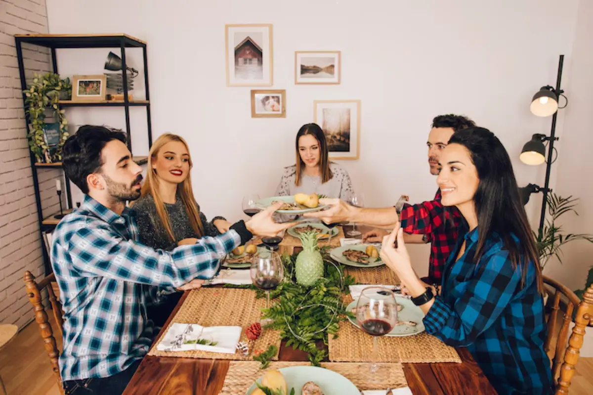 A group gathers around a beautifully set dining table, sharing dishes and enjoying each other's company amidst a cozy atmosphere.