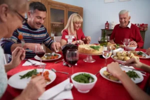 A festive dining table set with multiple dishes, wine glasses, and a cake, surrounded by people enjoying a meal together.