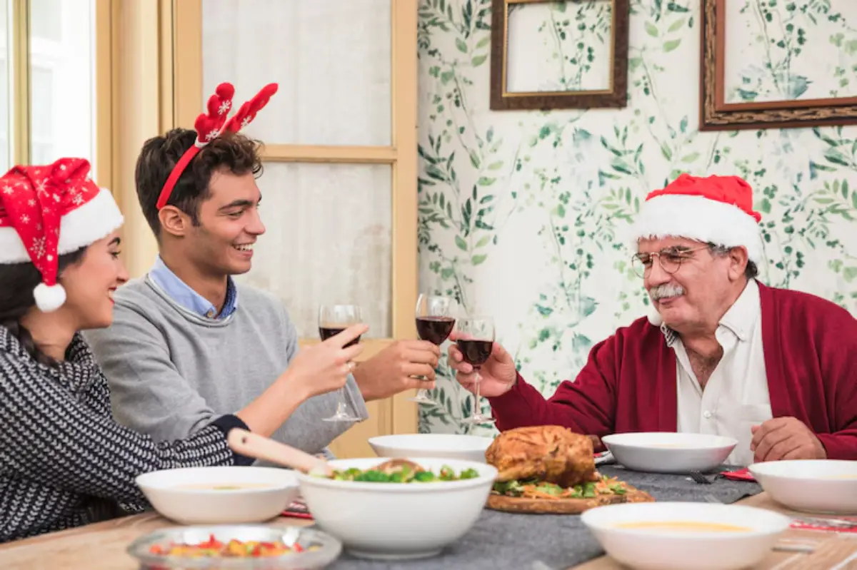 A festive holiday gathering with three people toasting with glasses of red wine at a table filled with various dishes and decorated with foliage.