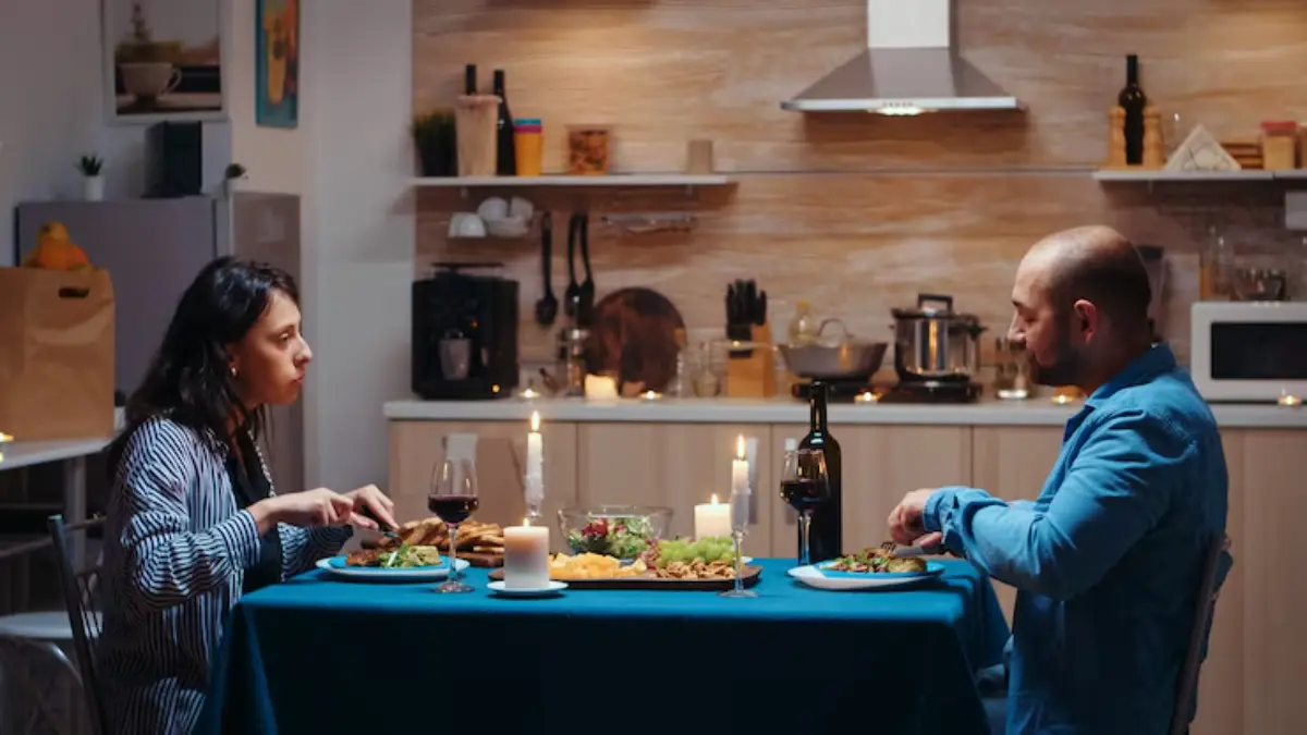A romantic dinner setup with two people, a blue tablecloth, candles, wine, and a variety of delicious dishes on the table.