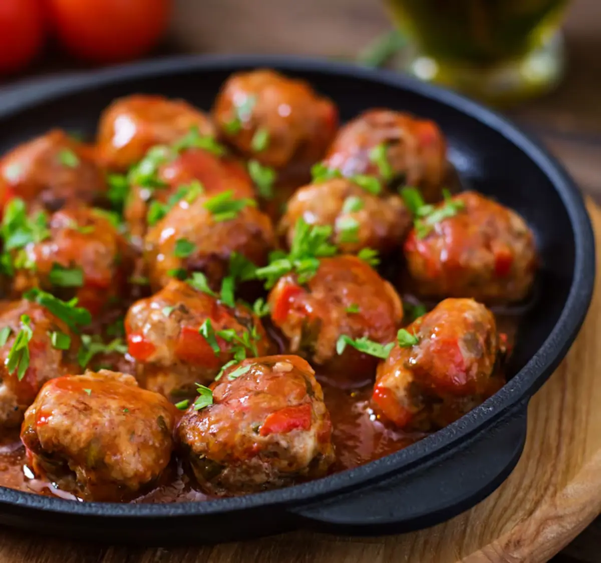 A skillet filled with savory meatballs, garnished with fresh parsley, in a rich red sauce with hints of bell pepper.