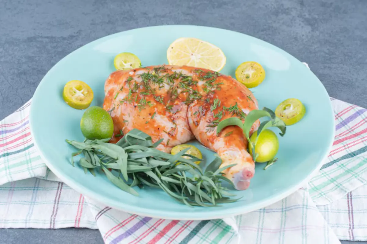 Grilled chicken leg glazed with sauce, garnished with fresh herbs and citrus slices, served on a turquoise plate.