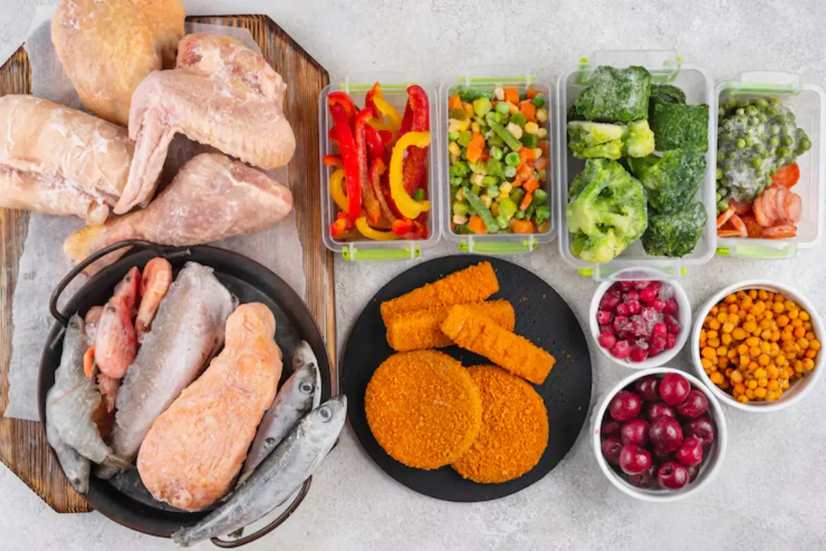A variety of frozen meats, vegetables, and fruits arranged on a counter, including fish, chicken, mixed veggies, berries, and crispy patties.
