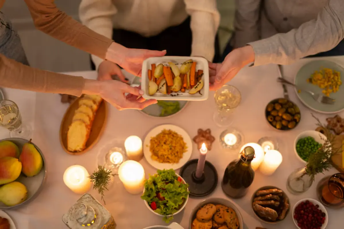A cozy dinner table with various dishes, including roasted vegetables, salad, and desserts, surrounded by candles and wine glasses.