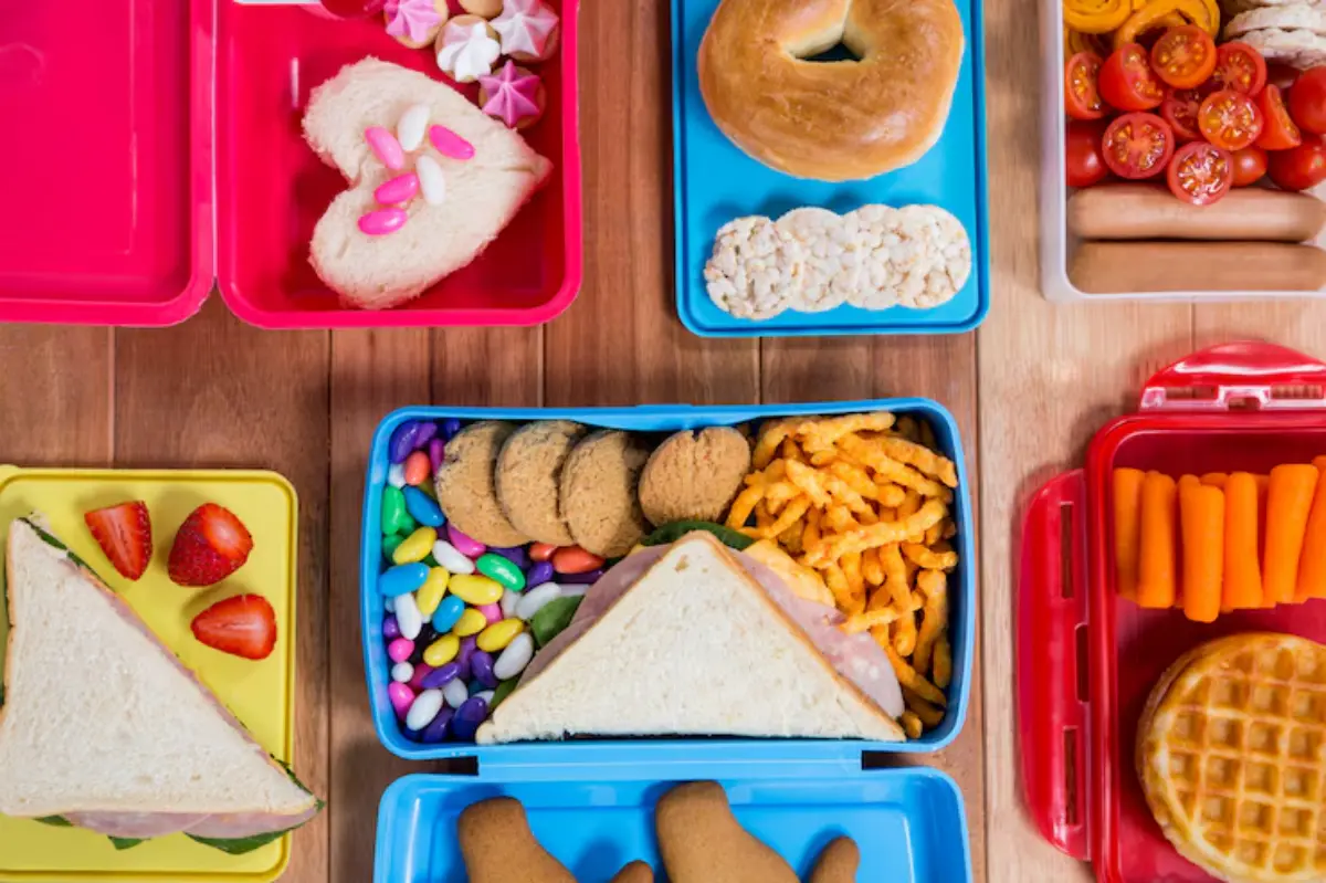 A colorful assortment of packed lunches in various containers, featuring sandwiches, fruits, snacks, and sweets.