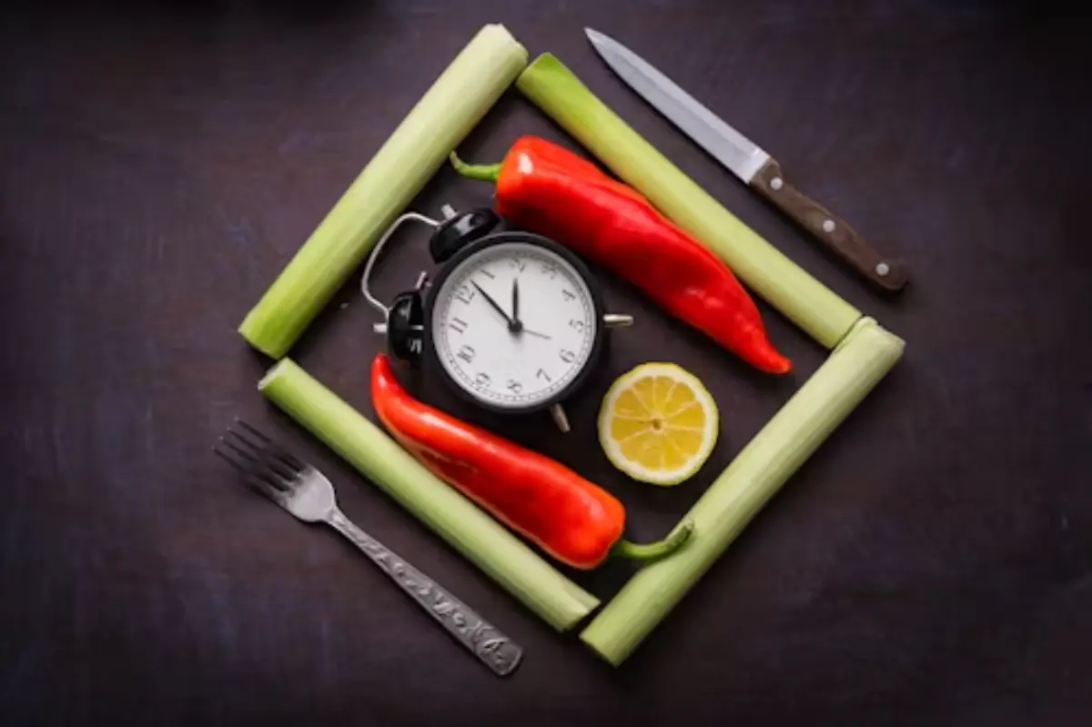 A clock, red chili peppers, a lemon slice, celery sticks, and a knife arranged artistically on a dark background.