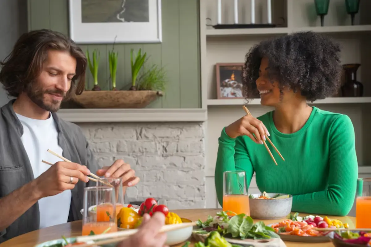 A dining table filled with colorful dishes, glasses of drinks, and two people sharing a meal with chopsticks.