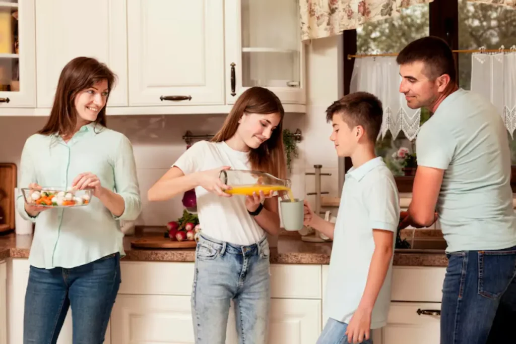 A family prepares food in a cozy kitchen, with one person pouring orange juice and others handling fresh ingredients.